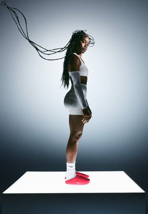 Atletyczna sylwetka ubrana w biały krótki top, rękawy na ramiona i czerwone korki Nike, stojąca na świecącej platformie, z długimi splecionymi warkoczami.