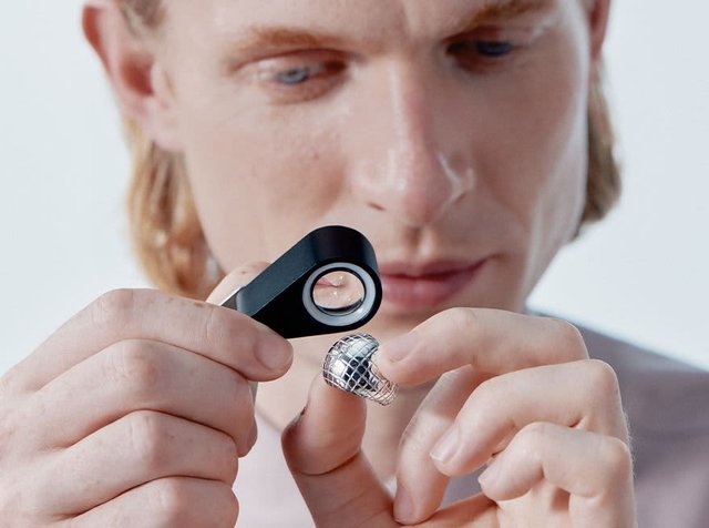 Μεγέθυνση με μαύρο σώμα που κρατιέται κοντά σε ένα σκουλαρίκι με ασημί υφή στα χέρια ενός ατόμου. Το σκουλαρίκι διαθέτει ένα μοτίβο σε πλέγμα.