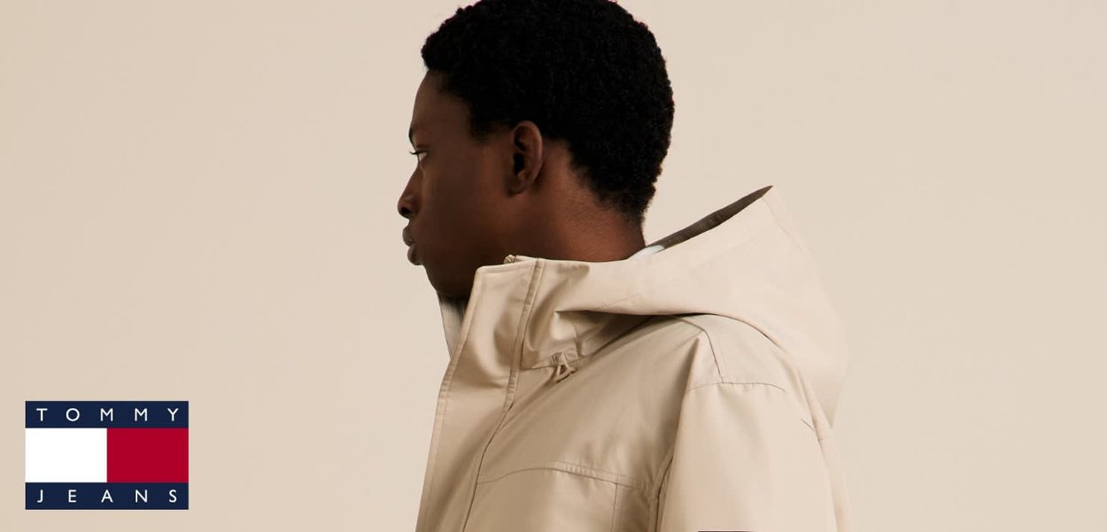 Giacca beige con cappuccio e trama liscia, con collo alto e cuciture visibili. Logo posizionato nell'angolo in basso a sinistra.