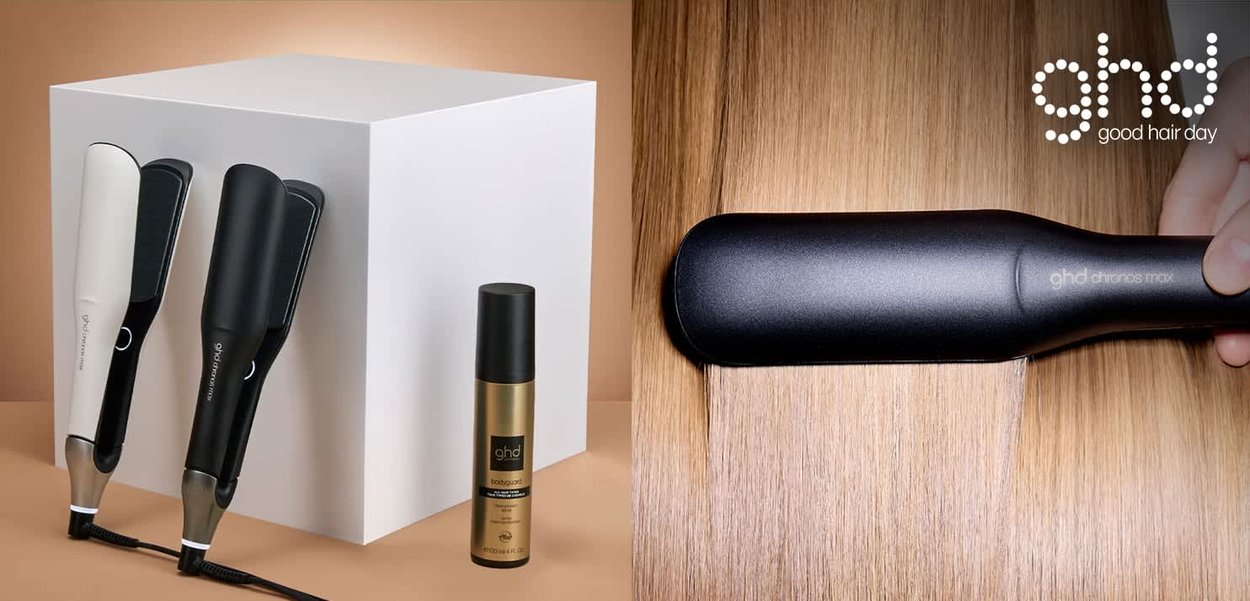 Twee GHD stijltangen, één wit en één zwart, naast een gouden sprayfles, tegen een lichte achtergrond met houten textuur.
