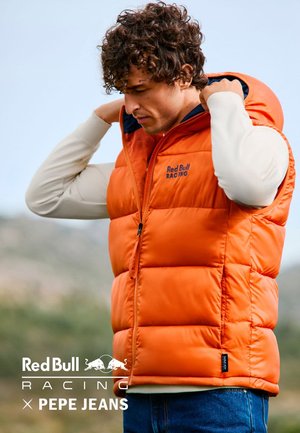 Oranger Steppweste mit Kapuze, ausgestattet mit einem Frontreißverschluss, Red Bull Racing-Logo und elastischen Bündchen. Wird über einem hellen Langarmshirt getragen.