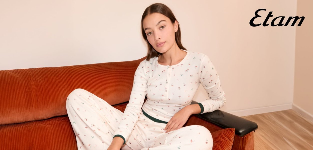 Weißer Pyjama mit langen Ärmeln und kleinen Blumenmustern, mit einem Knopfverschluss am Ausschnitt und grünem Taillenbund; präsentiert auf einer braunen Cordcouch.