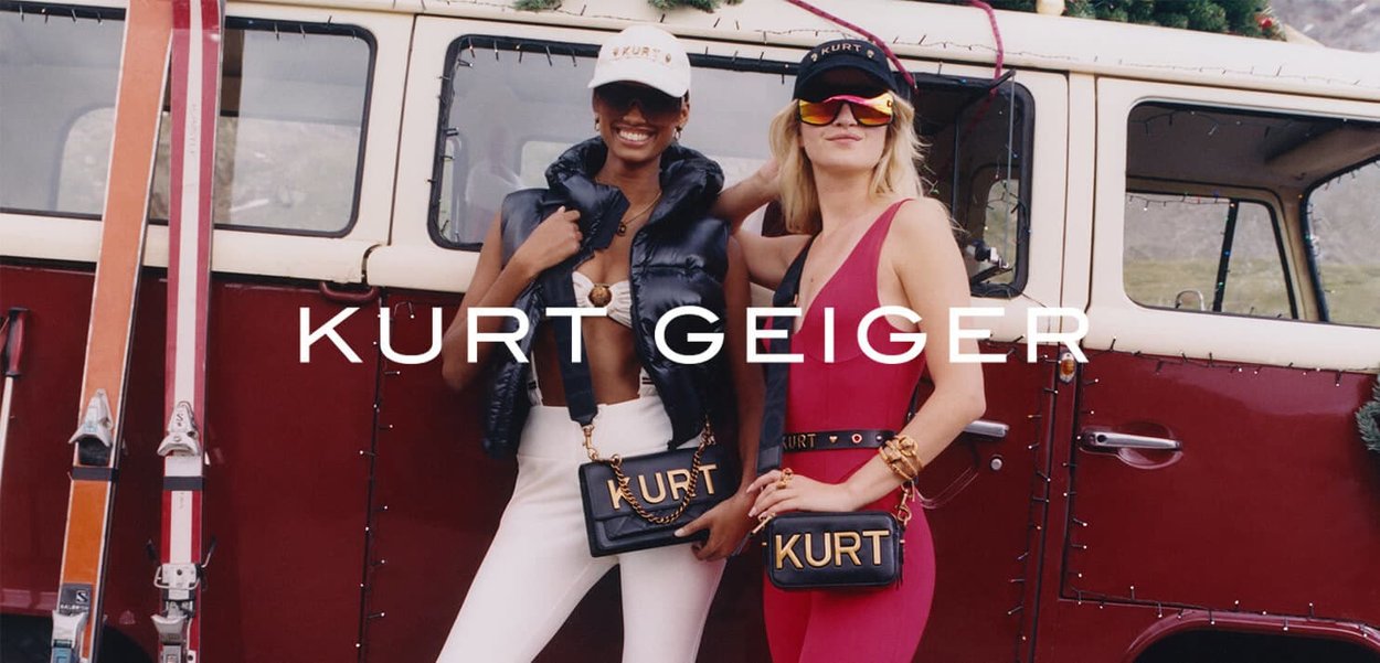 Deux mannequins posent devant une vieille camionnette rouge. Ils portent un gilet matelassé noir et une robe rouge, chacun tenant un sac noir avec l'inscription "KURT" en relief.