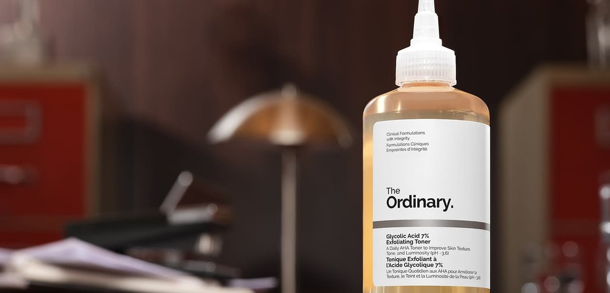 Bottiglia di The Ordinary Glycolic Acid 7% Exfoliating Toner con etichetta bianca su una superficie in legno, sfondo sfocato con lampada e mobili.