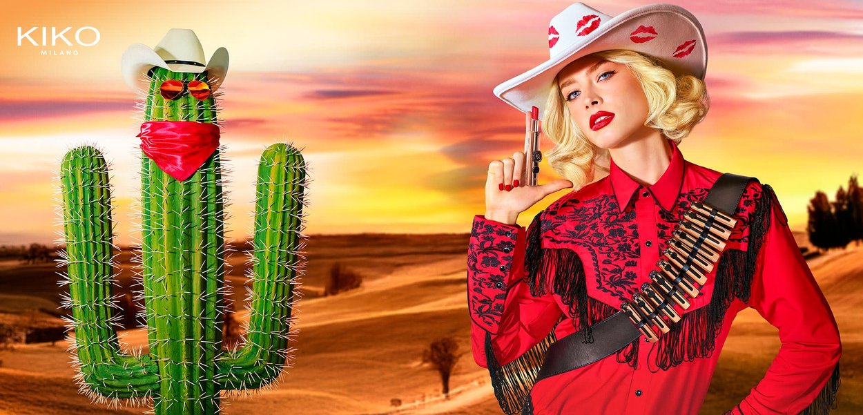 Red lipstick held by a person wearing a red embroidered shirt with black details. A large white hat features red kiss marks.