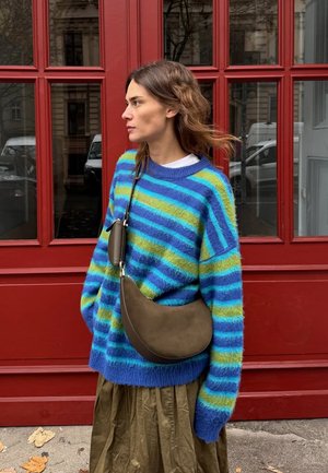 Übergroßer blauer und grüner gestreifter Pullover aus kuscheligem Material, kombiniert mit einer braunen, geschwungenen Schultertasche und einem plissierten olivgrünen Rock.