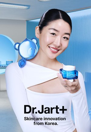 Crème Vital Hydra Solution de Dr. Jart+ dans un pot bleu, tenue par un mannequin. Un accessoire en forme d'ours bleu repose sur son épaule. Fini lisse et brillant.