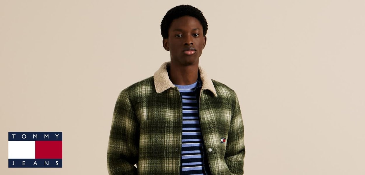 Giacca a quadri verde con colletto in sherpa color crema sopra una camicia a righe blu. Presenta bottoni frontali e una piccola toppa con il marchio.