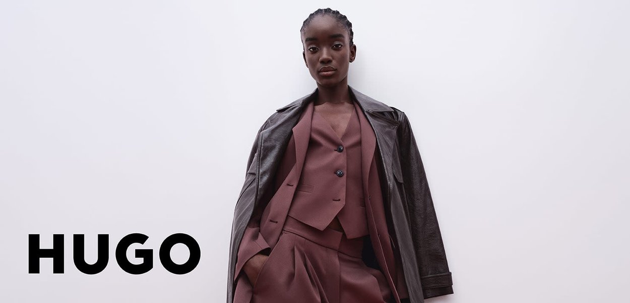 Traje estructurado burdeos con una chaqueta recortada y pantalones de pierna ancha, llevados bajo un abrigo de cuero oscuro. Textura suave con detalles de botones.