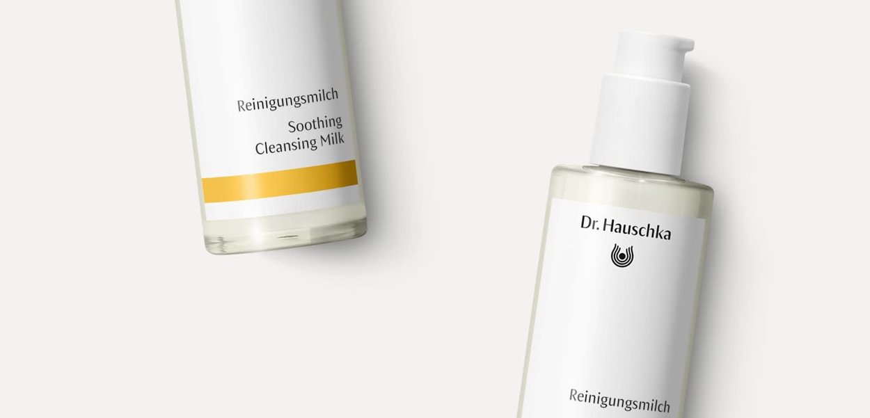 Zwei durchscheinende Flaschen Reinigungsmilch, eine weiße mit Pumpe, die andere mit gelben Akzenten, beschriftet mit "Beruhigende Reinigungsmilch".