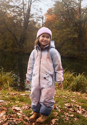 Børns vandtætte heldragt i pastelrosa og blå, med et enhjørning design. Bæres med en lyserød strikket hue og brune støvler.