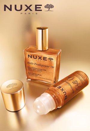 Flacon en verre doré de NUXE Huile Prodigieuse Or avec un bouchon doré. À côté, un petit flacon roll-on du même huile avec un applicateur transparent.