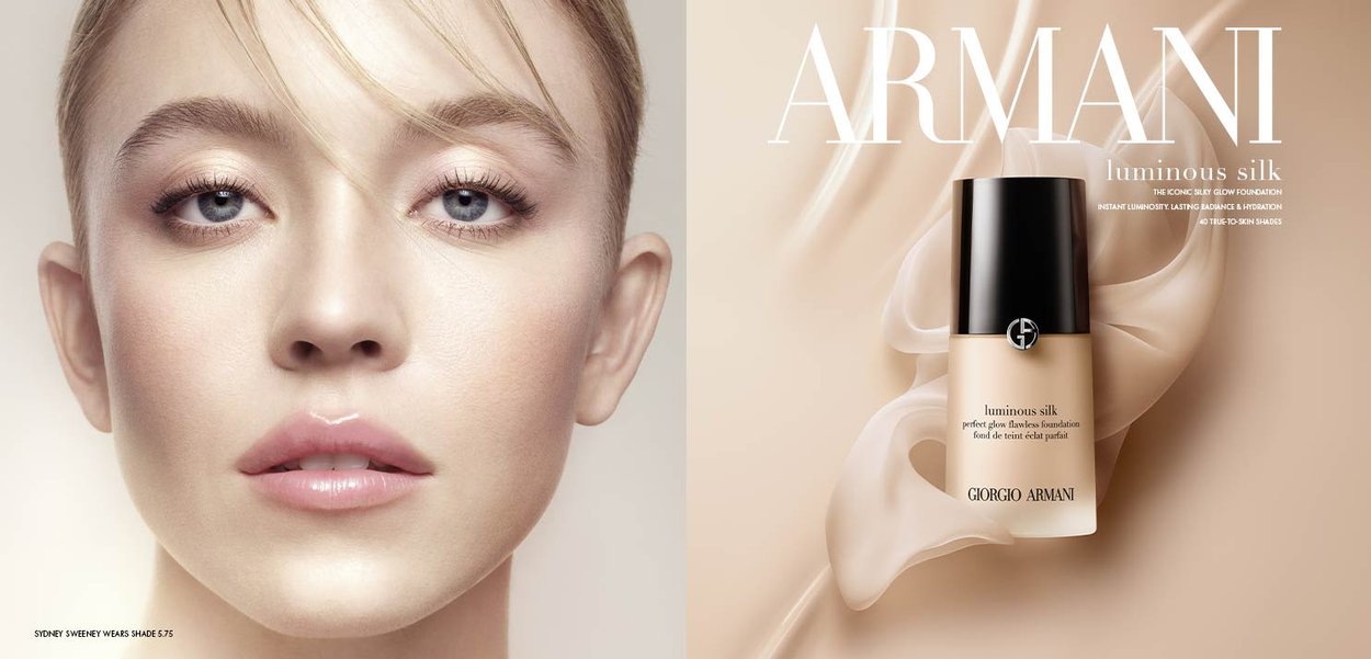 Showcases a bottle of "Luminous Silk" foundation with a sleek black cap and a beige body against a soft, wavy silk background.