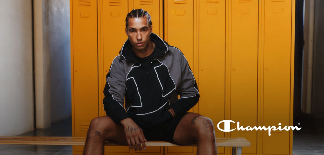 Schwarze und graue Sportjacke mit reflektierenden Akzenten, kombiniert mit schwarzen Shorts. Der Hintergrund zeigt gelbe Schließfächer und eine Holzbank.