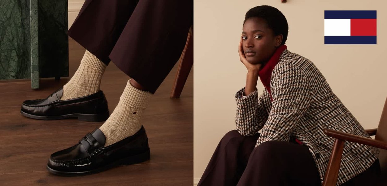Sittende kvinne i houndstooth-blazer, rød rullekravegenser, mørke bukser, kremfargede strikkesokker og svarte loafers ved siden av en Tommy Hilfiger-logo.