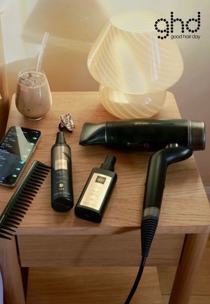 Houten tafel met een zwarte föhn, twee styling sprays, een zwarte kam, een haarclip, ijskoffie, een telefoon met alarmen en een gloeiende tafellamp.