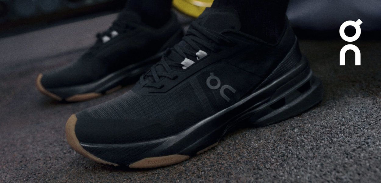 Schwarze Sportschuhe mit einer strukturierten Oberseite und Logodetails. Sie verfügen über eine gepolsterte Sohle mit einer hellbraunen Außensohle und mehreren Belüftungsrillen.