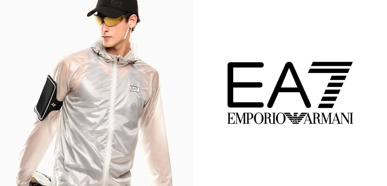 Uomo che indossa una giacca traslucida argento EA7 Emporio Armani, cappello nero, occhiali con lenti gialle e marsupio per smartphone, che guarda di lato.