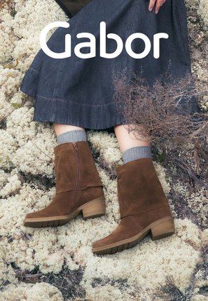 Brown suede ankle boots with a side zipper, chunky heel, and rounded toe. Pairing with grey ribbed socks and a denim skirt.