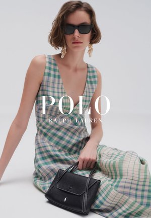 Mujer con gafas de sol negras, pendientes de concha y un vestido sin mangas de cuadros verdes, sosteniendo un bolso de cuero negro mientras está sentada.