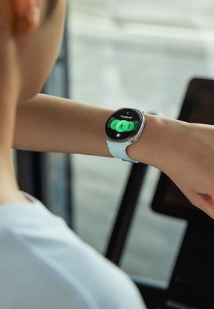 Person wearing a smartwatch with a white band, selecting the "Treadmill" workout mode on the watch display.