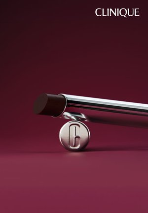 Clinique lippenstift met een donkerbruine tint, rustend op een ronde zilveren dop met een letter C erop, op een donkere bordeauxrode achtergrond.