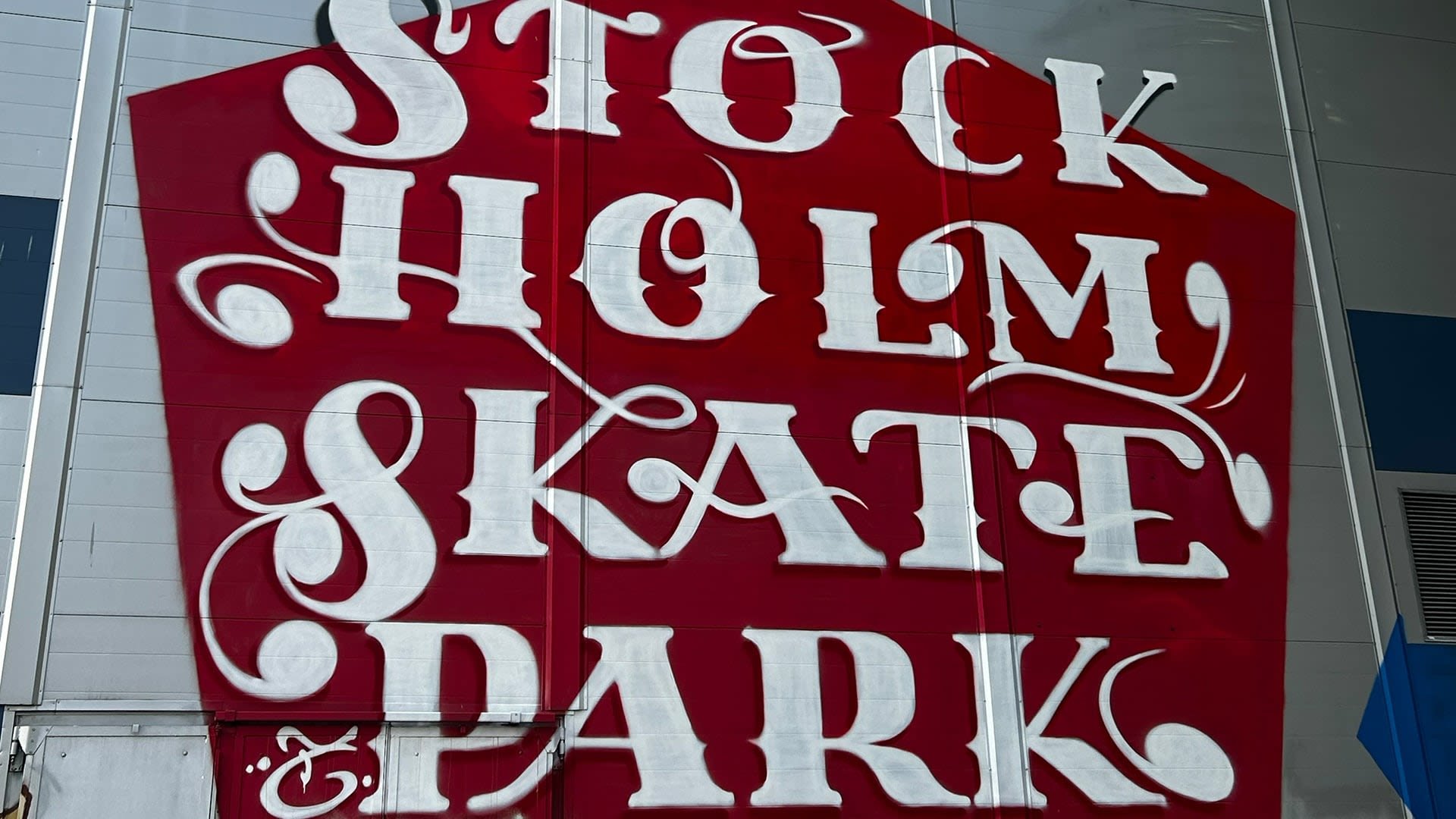 Rode muurschildering met grote witte letters die "STOCKHOLM SKATE PARK" leest, met een gedetailleerd, gestileerd lettertype. Eenvoudig ontwerp, zonder extra details.
