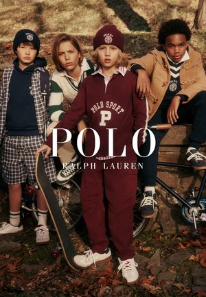 Vier Kinder in herbstlicher Außenumgebung, gekleidet in Polo Ralph Lauren Kleidung, eines hält ein Skateboard, ein anderes hat die Hand am Fahrrad, alle schauen nach vorne.