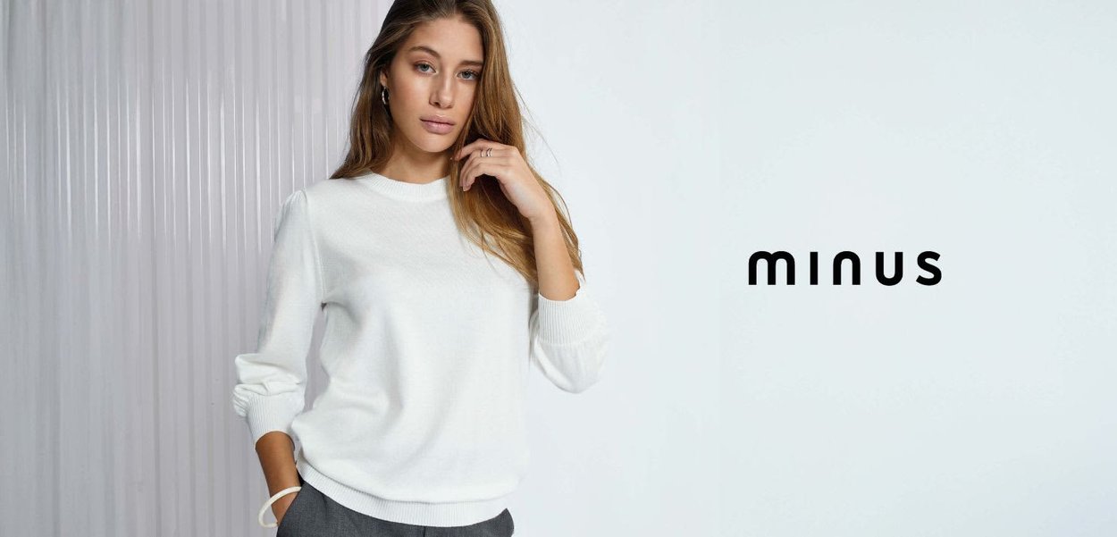 Pull en tricot blanc avec un col en côtes et des poignets, associé à un pantalon gris, au design sans couture et à la coupe décontractée. Texte de la marque "minus" affiché.