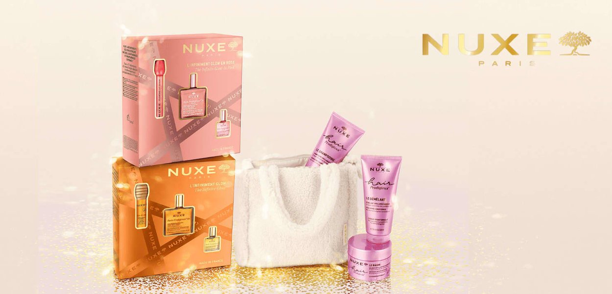 Set di prodotti NUXE con due confezioni regalo in rosa e arancione con dettagli dorati; include una borsa bianca in peluche e tre prodotti per la cura dei capelli rosa.