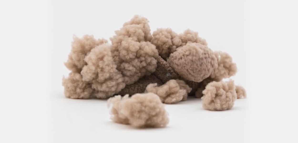 Braune, strukturierte Fasern, die weichen, flauschigen Klumpen ähneln und unregelmäßig angeordnet sind, wodurch ein natürliches, organisches Aussehen mit unterschiedlichen Größen und Formen entsteht.