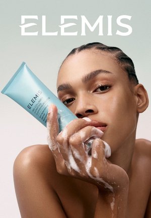 Kvinne med flettet hår holder et skummende rør med Elemis Pro-Collagen Hydro-Radiance Cleansing Mousse nær ansiktet.