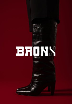 Schwarzer kniehoher Stiefel aus strukturiertem Leder mit spitzer Zehe, schmalem Absatz und gerafftem Design. Deutlich sichtbare Markenaufschrift "BRONX".