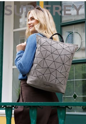 Zaino grigio con motivo geometrico e superficie strutturata, dotato di manico superiore e dettaglio con marchio alla base, indossato sulla schiena.