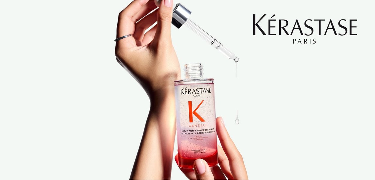 Kérastase Genesis serum i en klar glasflaske med et sølvfarvet pipette låg. Serumet er lyserødt med bobler og har en fremtrædende etikette.