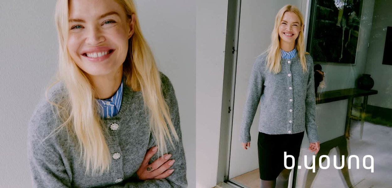 Cardigan grigio lavorato a maglia con bottoni tondi e una consistenza morbida, indossato sopra una camicia a righe blu e bianche, abbinato a una gonna scura.