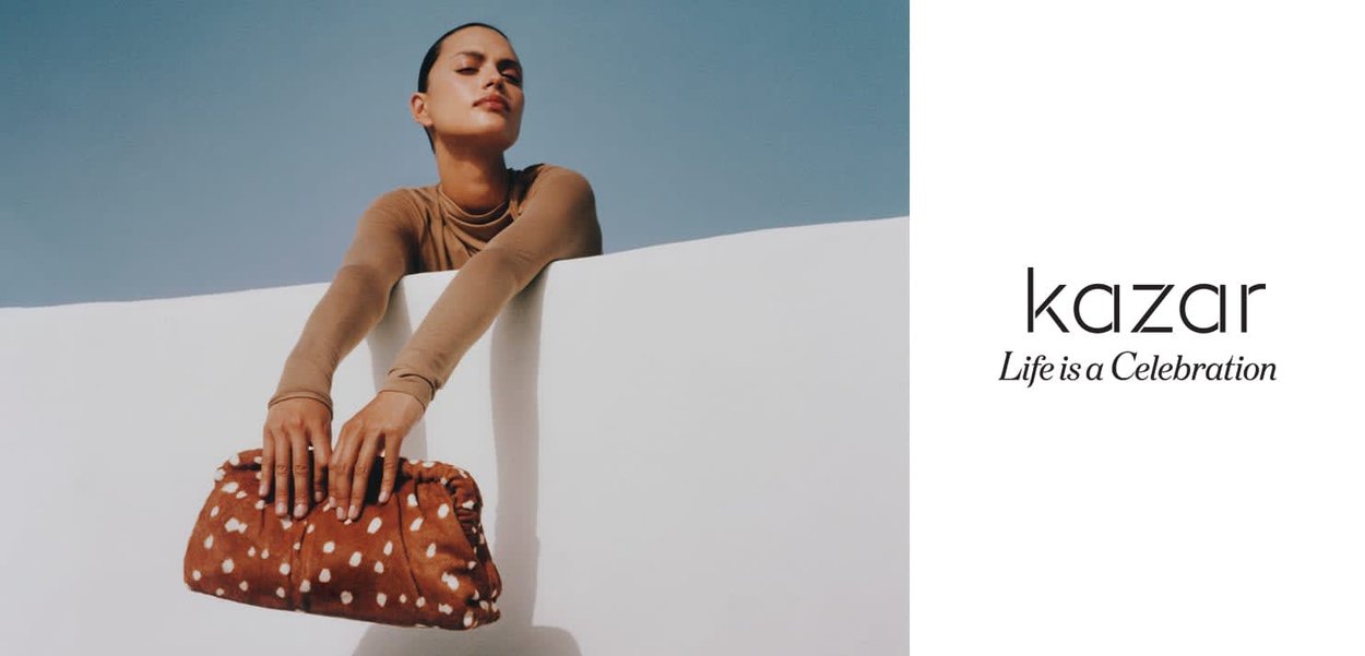 Brown polka dot clutch purse made of soft fabric, softly gathered at edges, held by a person against a solid white background.