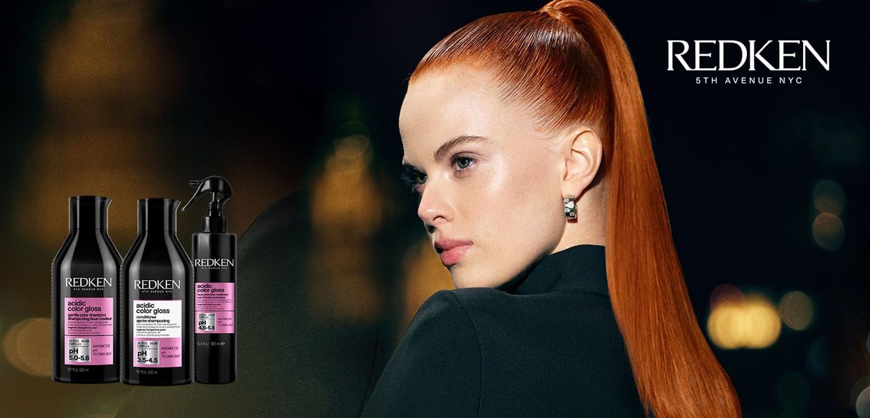 Three Redken shampoo and conditioner bottles in black with pink labels, accompanied by a black spray bottle, set against a gradient background.