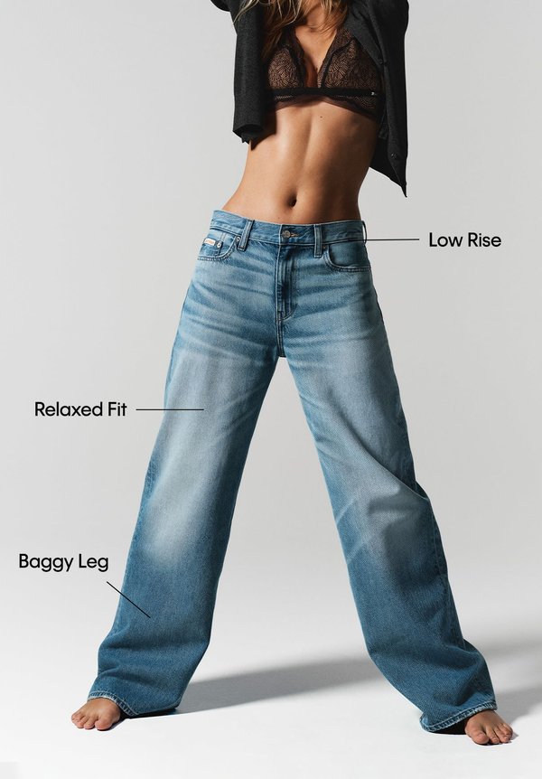 Jean denim de color azul claro con tiro bajo, corte relajado y perneras anchas. Presenta una textura suave y zonas desgastadas cerca de los bolsillos.