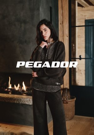 Dunkelbrauner, strukturierter Langarm-Pullover mit silberner Akzentuierung und hohem Kragen, kombiniert mit passenden weiten Hosen. "Pegador"-Logo sichtbar.