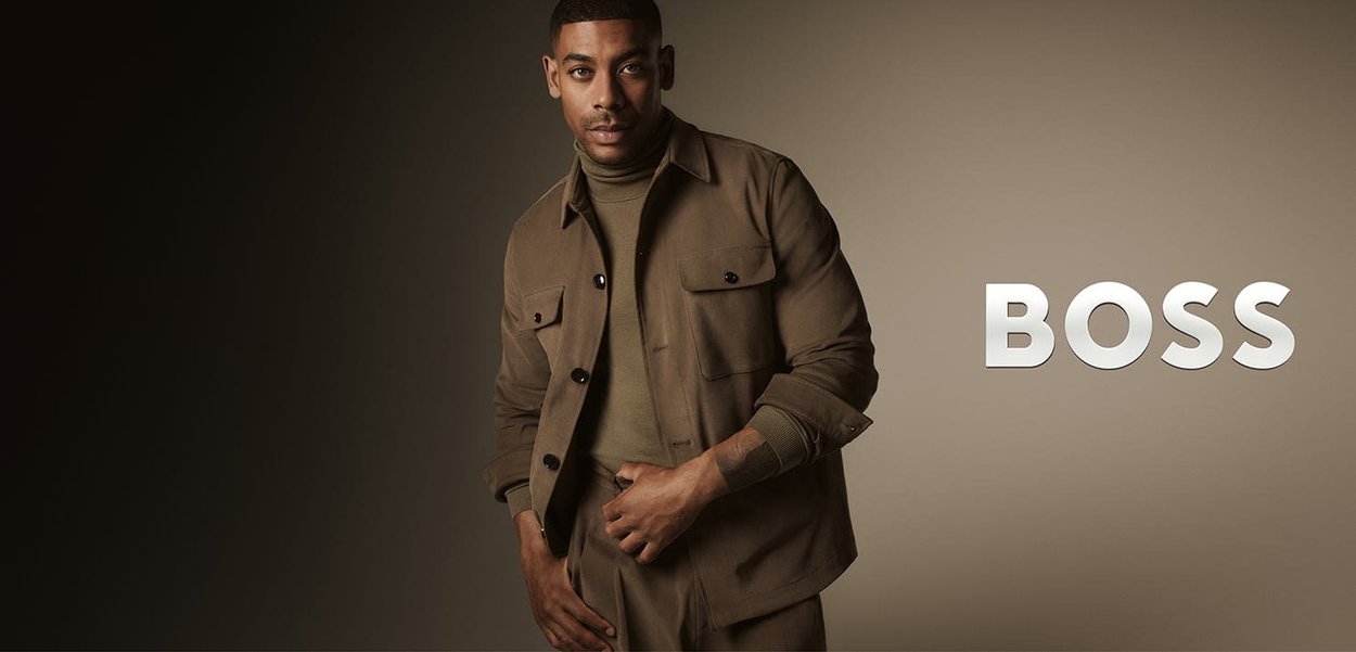 Braune Button-Down-Jacke über einem grünen Rollkragenpullover, mit aufgesetzten Taschen, strukturiertem Stoff und lässiger Passform vor einem Verlaufshintergrund.