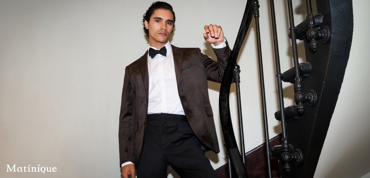 Brauner Samt-Sakkosegment über einem weißen Hemd, kombiniert mit schwarzen Hosen. Das Modell posiert auf einer schwarzen Wendeltreppe mit kunstvollen Geländern.