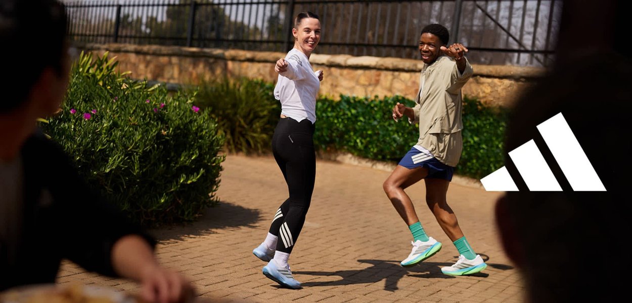 Una mujer y un hombre corriendo al aire libre por una acera junto a un muro de ladrillos al atardecer, vestidos con ropa deportiva y zapatillas de correr.