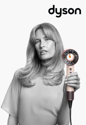 Donna con capelli acconciati che tiene un asciugacapelli Dyson rosa rivolto in avanti, mostrando il meccanismo interno e i controlli.