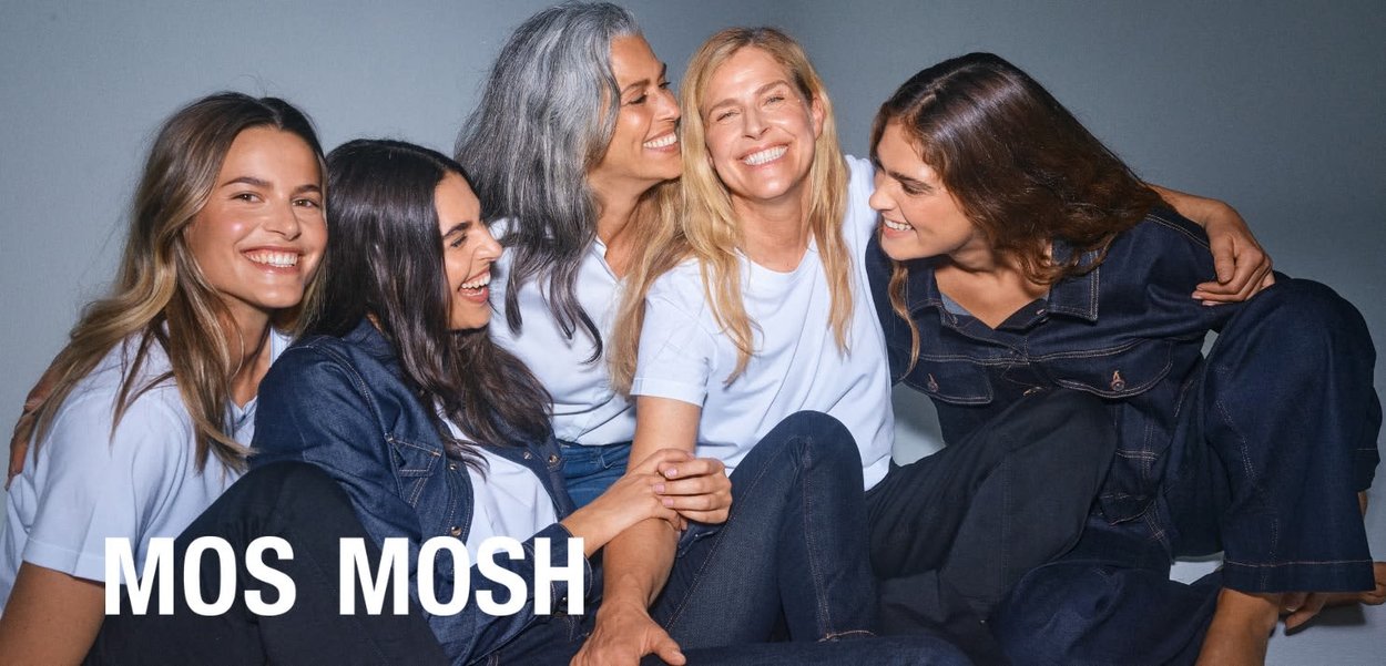 Fem smilende kvinder iført casual denim og hvide toppe, sidder tæt sammen mod en grå baggrund med "MOS MOSH" tekst.