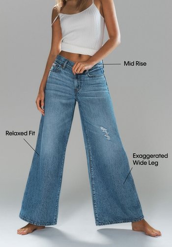 Jeans de mezclilla azul claro con cintura de media altura, corte relajado y pierna ancha exagerada. Presenta un detalle desgarbado en una pierna.
