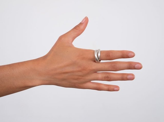 Λαμπερός στριμμένος μεταλλικός δακτυλίδι σε χέρι, που εμφανίζεται με τα δάχτυλα ελαφρώς ανοιχτά, αναδεικνύοντας την ομαλή υφή και την γυαλιστερή φινίρι σε ένα ουδέτερο φόντο.