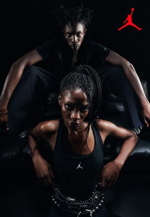 Dwóch czarnoskórych mężczyzn ubranych w czarną odzież z logo Jordana, pewnie pozujących na czarnej skórzanej sofie na ciemnym tle.