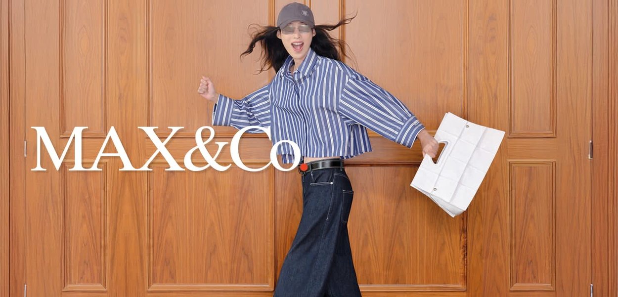 Donna con maglietta a righe e cappellino che cammina gioiosamente, tenendo una borsa a tracolla bianca, in piedi davanti a una parete rivestita in legno.