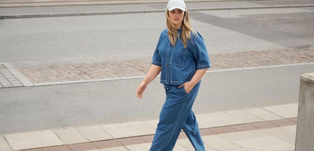 Blårandig denimoutfit bestående av en kortärmad skjorta och löst sittande byxor, ihop med en vit basebollkeps.